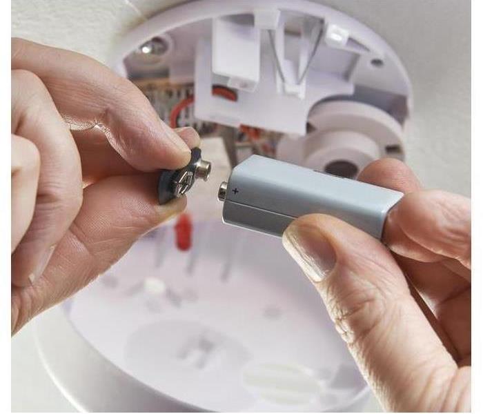 A hand installing a battery in a fire alarm